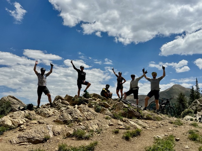 Riders celebrating with arms raised on a rocky high point