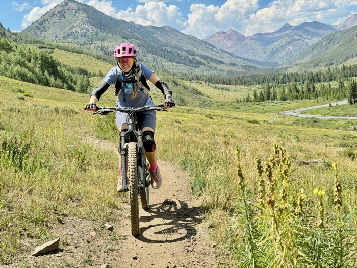 A rider riding toward the camera on a valley trail below red rock peaks